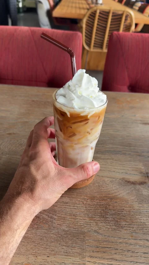 Hand Holding Iced Coffee with Whipped Cream in Cozy Café (Vertical) Stock Footage 340540915
