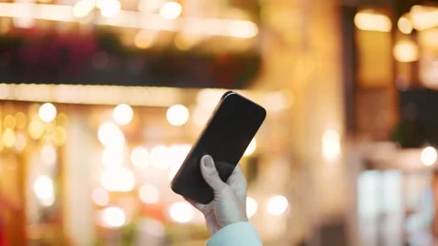 Hand holding iPhone 16 in front of night lights in city Stock Footage 287864200