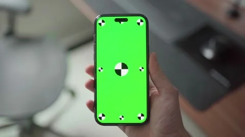 Hand holding an iPhone 16 Pro Max with a green screen in a modern office setting Stock Footage 295131674