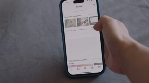 Hand holding an iPhone scrolling over Fiverr app. Finger touching iPhone screen Stock Footage 306005754