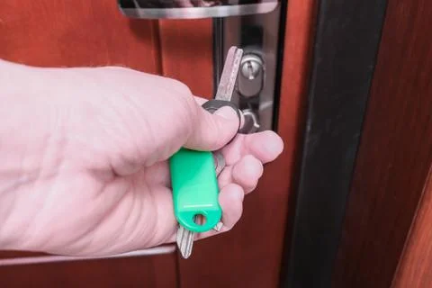 A hand holding a key and inserting it in a keyhole in order to open or lock a Stock Photos