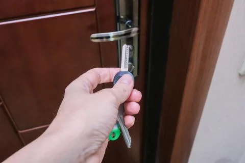 A hand holding a key and inserting it in a keyhole in order to open or lock a Stock Photos