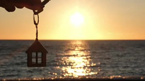 Hand holding key with house shaped keychain on background of sea sunset Stock Footage 301848735