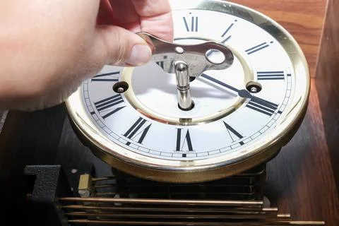 A hand holding a key to wind up a clockwork, vintage classic clock mechanism Stock Photos