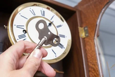 A hand holding a key to wind up a clockwork, vintage classic clock mechanism Stock Photos
