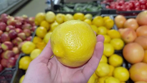 Hand holding a large yellow lemon in a grocery store produce section 库存影片 340998108