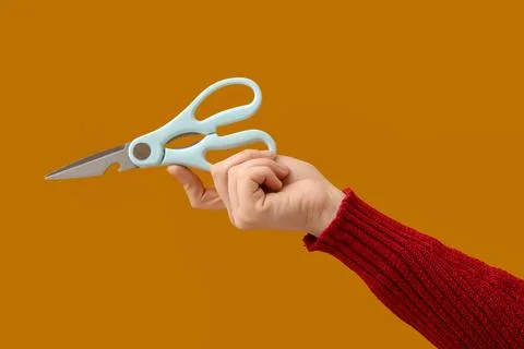 Hand holding light blue kitchen shears with bottle opener feature on warm ora Stock Photos