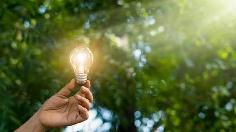 Hand holding light bulb bright light on green nature background,  Ecology Stock Photos