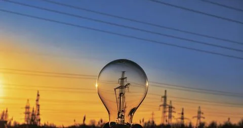 Hand holding light bulb in front of high voltage post, energy sources for ren Stock Photos