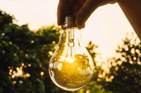 Hand holding a light bulb with sunset power concept power the future Stock Photos