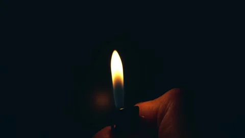 A hand holding a lighter, igniting a flame against a dark background Vidéo 305996185