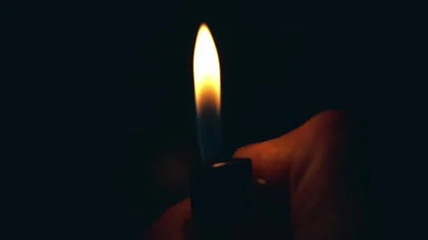 A hand holding a lighter, igniting a flame against a dark background Stock-Footage 305996190