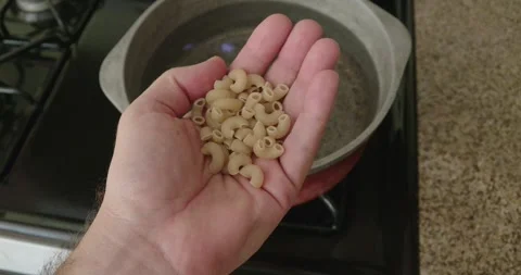 Hand Holding Macaroni Over Pot of Water in a kitchen Stock Footage 311070944