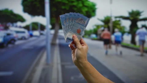 Hand holding malaysian ringgit notes on an urban street with blurred people.. Stock Footage 303423957