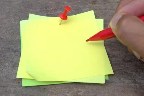 Hand holding a marker to write on a yellow Stiki note attached to a wooden .. Stock Photos