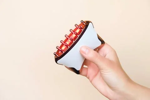 Hand holding a microcurrent massage device with therapeutic red light mode on Stock Photos