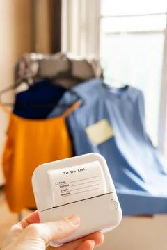 Hand holding mini thermal printer with clothing decluttering checklist in b.. Stock Photos