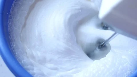 Hand-holding a mixer and making homemade whipped cream in a bowl, close up Stock Footage 253437787