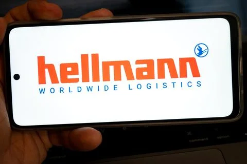 Hand holding mobile device displaying hellmann worldwide logistics brand 写真素材