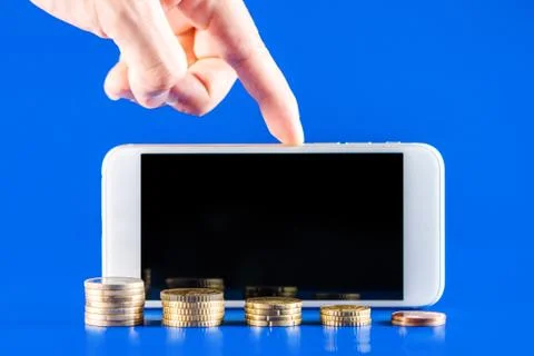 Hand holding a mobile phone with stack of coins on blue background. Business  Stock Photos