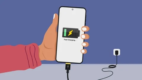 Hand holding a mobile phone while charging the battery from wall outlet Stock Footage 334665206