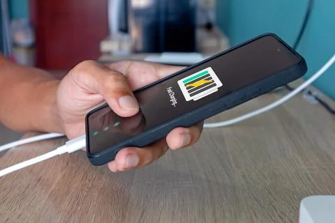 Hand holding a mobile phone while charging the battery from wall outlet Stock Photos