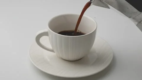 Hand holding Mokapot pouring coffee into white cup on table.  Stock Footage 242829088