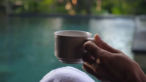 A hand holding a mug with coffee on the background of private swimming pool Stock Footage 154165984