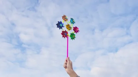 Hand holding multiple colorful transfer windmill toy against blue sky 스톡 동영상 292157441