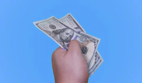 Hand holding multiple prop dollar bills against a blue background Stock Photos