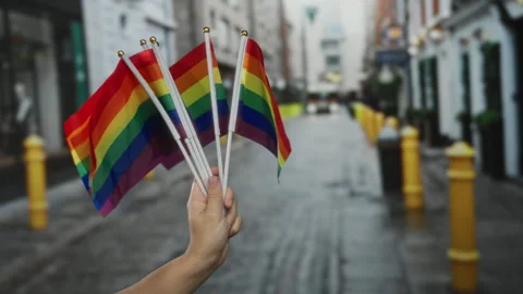 Hand holding multiple rainbow flags on a city street signifies lgbtq pride .. 스톡 동영상 310637266