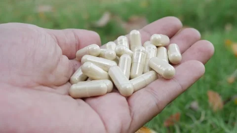 Hand holding multiple white herbal supplement capsules Видео 330764194