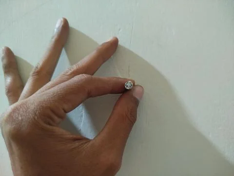 Hand holding a nail embedded in the white cement wall 스톡 사진