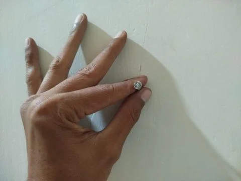 Hand holding a nail embedded in the white cement wall 스톡 사진