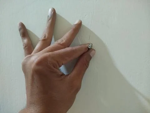 Hand holding a nail embedded in the white cement wall Photos