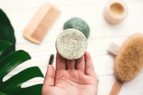 Hand holding natural solid shampoo bar on background of bamboo brush, deodora 스톡 사진