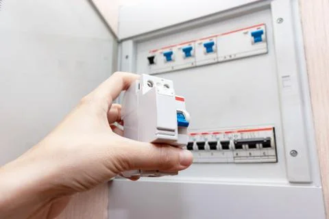 Hand holding new automatic switch and blurred electrical shield with automati Stock Photos