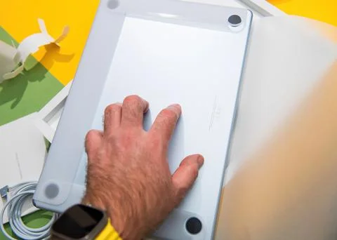 Hand holding new silver MacBook Air laptop unboxing on colorful Stock Photos