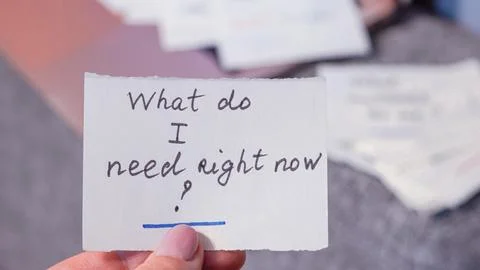 Hand holding note with question about needs, blurred background of papers Stock Photos