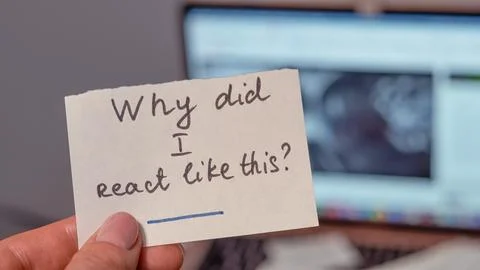 Hand holding note with question about emotional reaction, computer in backg.. Foto stock