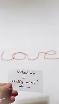 Hand holding note with question above string spelling love on white backgroun Stock Photos