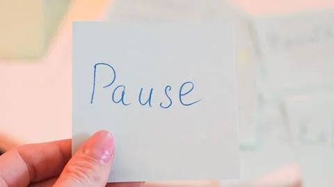 Hand holding a note with the word Pause written in blue ink on a light back.. Stock Photos