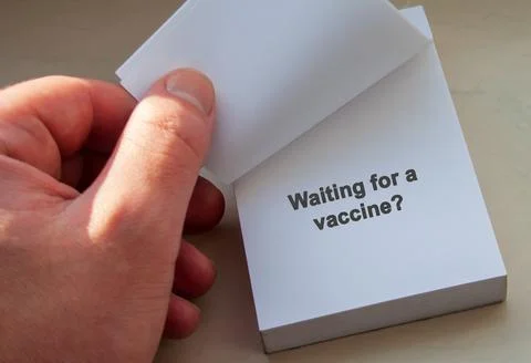 A hand holding a notepad displaying the phrase Waiting for a vaccine? The image Stock Photos