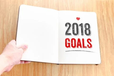 Hand holding open notebook with 2018 goals lay it on wooden table,Resolutions Foto stock