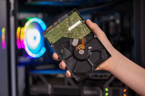 Hand holding opened hard disk drive in front of gaming computer with RGB li.. Stock Photos