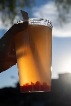 Hand holding orange bubble tea against sunny sky Stock Photos