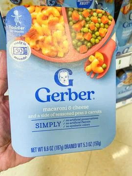 A hand holding a package of Gerber macaroni and cheese toddler meal with pe.. Stock Photos