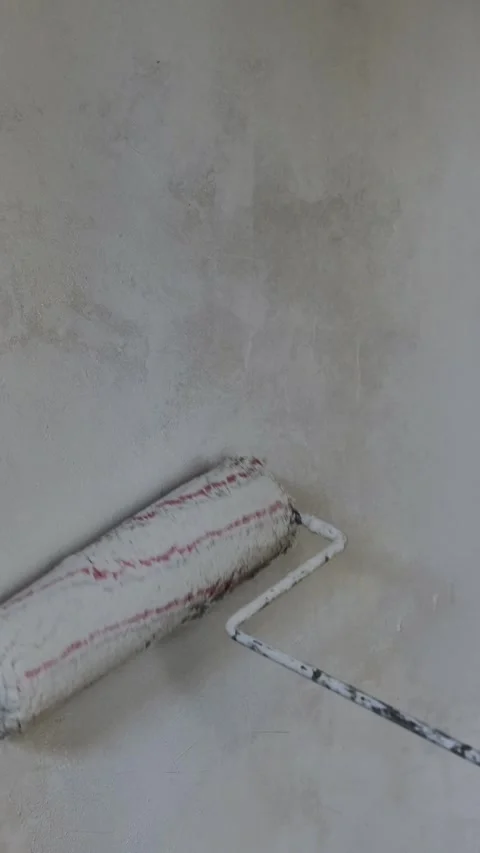 Hand holding a paint roller and applying fresh white paint on a concrete wall. Video stock 287645517