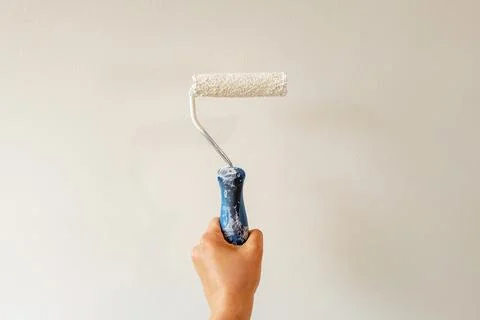 Hand holding paint roller applying white paint on interior wall Foto stock