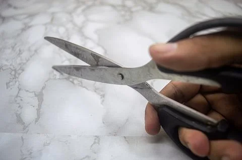 Hand holding a pair of sharp scissors over marble surface, emphasizing cont.. Foto stock